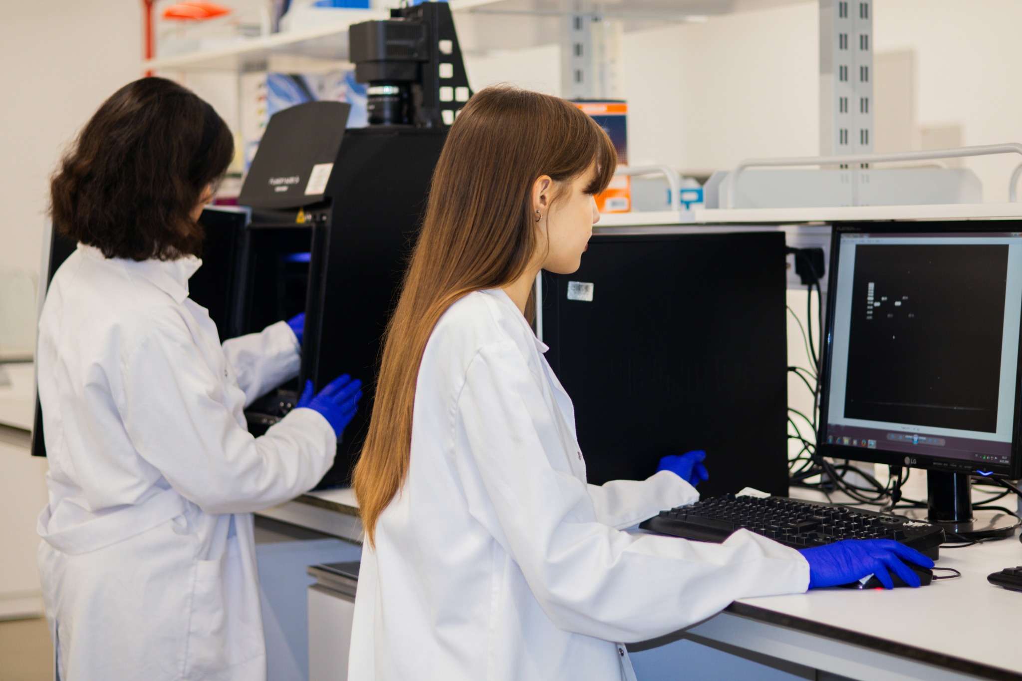 Two laboratory professionals working with imaging equipment and a computer