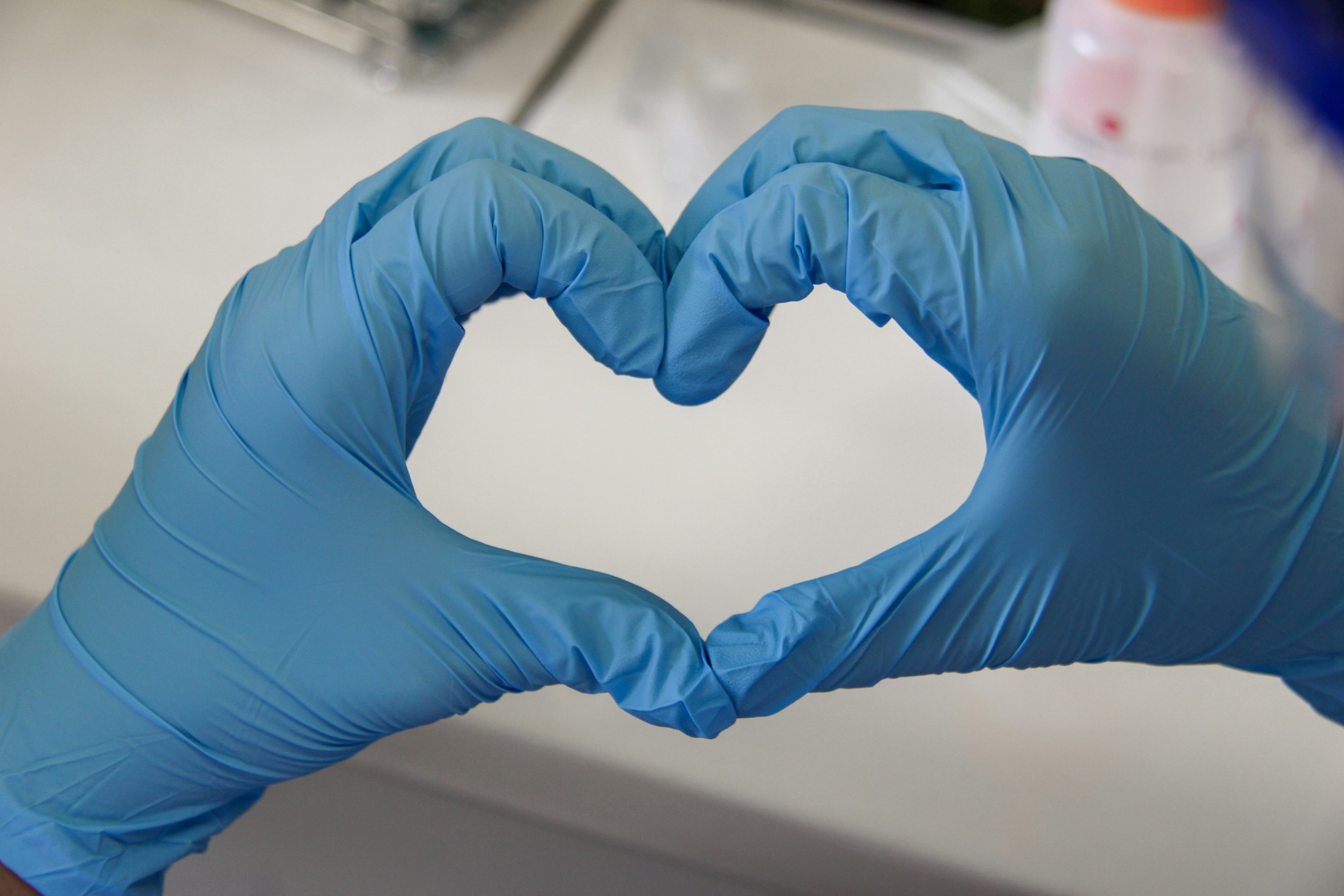 Two blue-gloved laboratory workers form a heart shape with their hands